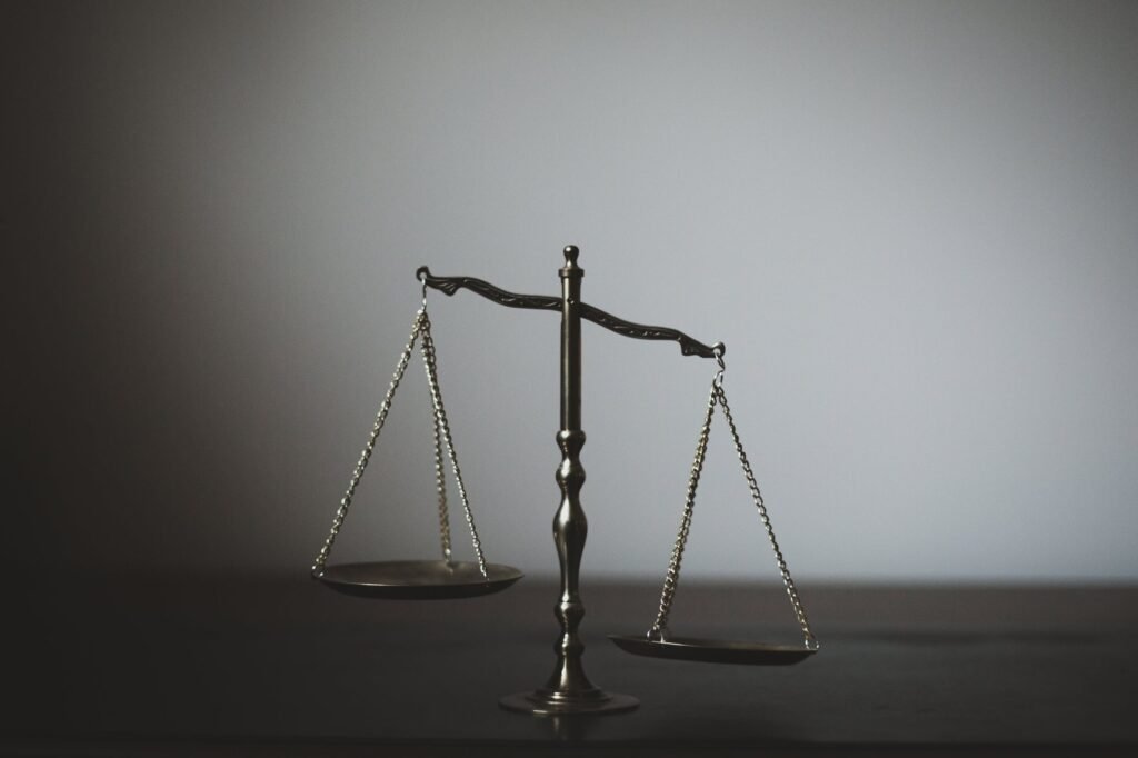 A metal balance scale standing on a dark surface against a plain grey background.